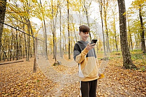 Teenage boy looking in mobile phone at autumn forest