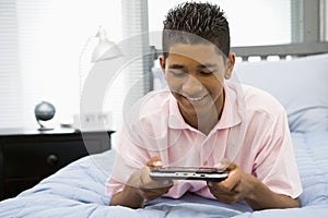 Teenage Boy Lying On Bed Playing Video Game