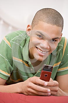 Teenage Boy Lying On Bed Using Mobile Phone