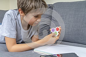 Teenage boy lying on the couch and playing with sensory pop it fidget toy at home. Kid playes stress and anxiety relief