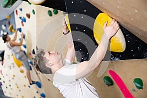 Teenage boy climbs steep artificial wall in sports complex and trains endurance