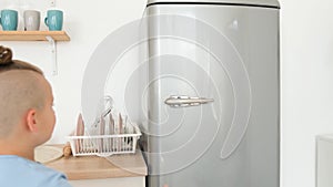 Teenage boy opens the refrigerator in the kitchen. Empty refrigerator, shortage of food