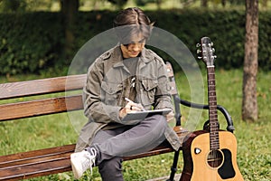 Teenage boy painting in tablet using pencil. Young designer using tablet outdoor. Autumn time. Background of guitar