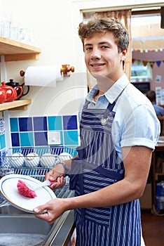 Teenage Boy With Part Time Job Washing Up In Coffee Shop