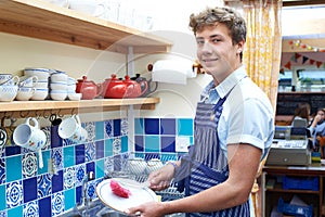 Teenage Boy With Part Time Job Washing Up In Coffee Shop