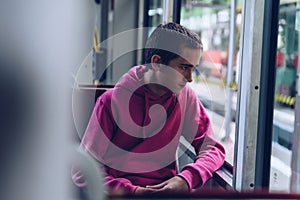 Teenage boy in a pink hooded sweatshirt, pensive s traveling by bus