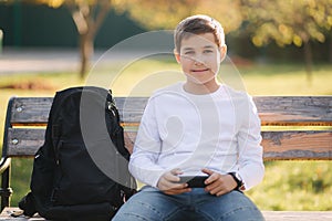 Teenage boy play online games on his smartphone in the park after lessons in school