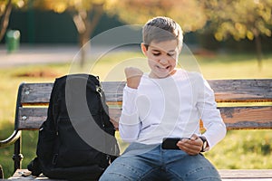 Teenage boy play online games on his smartphone in the park after lessons in school