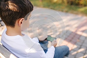 Teenage boy play online games on his smartphone in the park after lessons in school