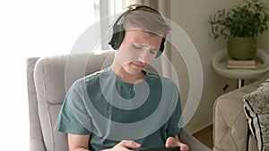 Teenage boy is playing a portable game console. A teenager sits in a chair in the living room and plays a gadget