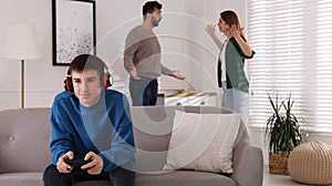 Teenage boy playing videogame while his parents arguing on background. Problems at home