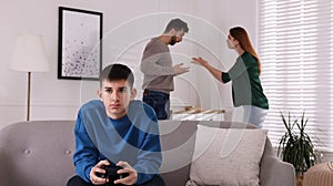 Teenage boy playing videogame while his parents arguing on background. Problems at home