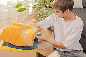 Teenage boy preparing itemsfor charity and packing into donation box at home. Donations for charity, help low income