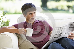 Teenage Boy Relaxing On Sofa With Newspaper And Drink