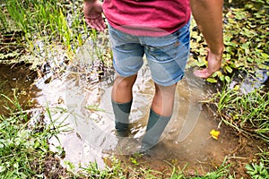 Teenage boy in rubber boots standing in lake.