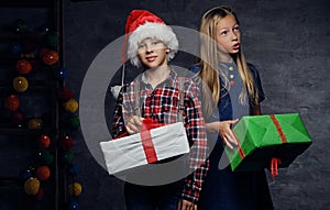 Teenage boy in Santa`s hat and blonde girl holds gift boxes.