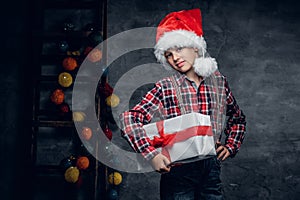 Teenage boy in Santa`s hat holds gift box.