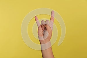 Teenage boy showing rock gesture on yellow background, closeup