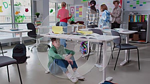 Teenage boy sit and cry under desk in classroom