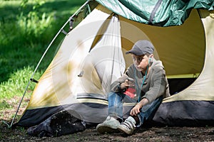 Teenage boy sits near a tent on a green meadow