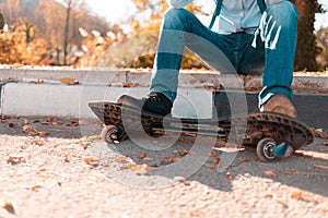 A teenage boy sits on a step with his feet on a skateboard. Street in the background. Close up and copy space