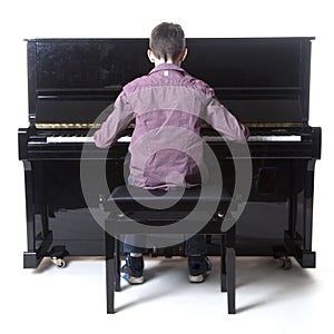 Teenage boy sits at upright piano in studio