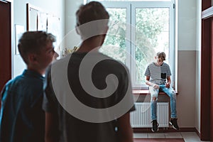 Teenage boy sitting alone at school, bullying among children concept