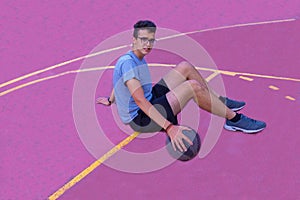 Teenage boy sitting on the court with a basketball