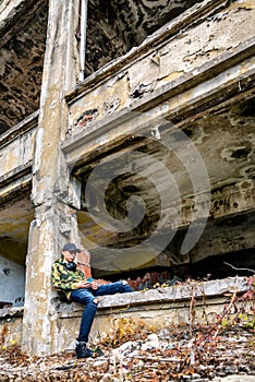 Teenage boy sitting on a crumbling building and using smarthphone