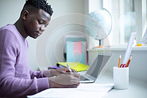 Teenage Boy Sitting At Desk Doing Homework Assignment On Laptop photo