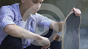 Teenage boy sitting lonely with skateboard, bored without friends, outsider