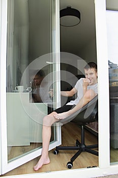 A teenage boy is sitting in an open door and is sad, looking in front of him