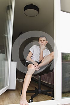 A teenage boy is sitting in an open door and is sad, looking in front of him