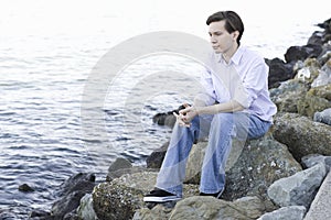 Teenage Boy Sitting On Rocks By Ocean