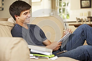 Teenage Boy Sitting On Sofa At Home Doing Homework