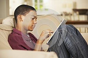 Teenage Boy Sitting On Sofa At Home Using Tablet Computer