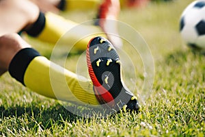 Teenage Boy Sitting and Stretching on Sports Grass Field. Soccer Ball in the Background