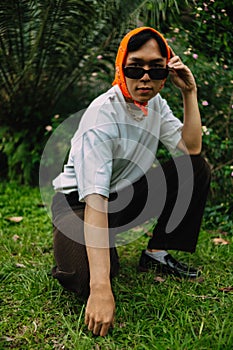 a teenage boy is sitting in sunglasses and an orange bandana in a park