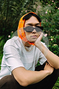 a teenage boy is sitting in sunglasses and an orange bandana in a park