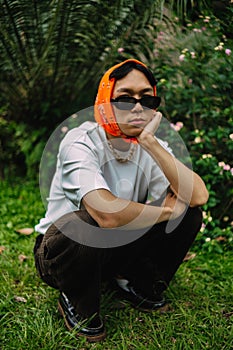 a teenage boy is sitting in sunglasses and an orange bandana in a park