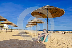 A teenage boy sitting under reed umbrella on the beach