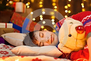 Teenage boy sleeping in new year or christmas decoration. Holiday lights, gifts and christmas tree decorated with toys