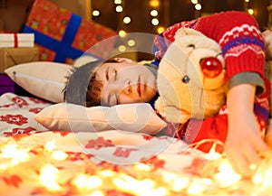 Teenage boy sleeping in new year or christmas decoration. Holiday lights, gifts and christmas tree decorated with toys