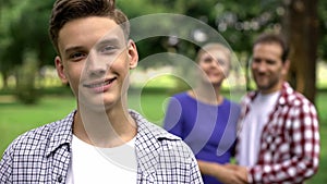 Teenage boy smiling on background of cheerful hugging parents, supporting family