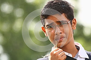 Teenage boy with specs biting grass blade