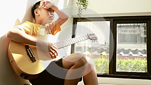 Teenage boy spends his favorite pastime. and free time to enjoy playing guitar at the foot of the stairs of the house.