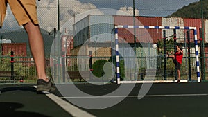 Teenage boy stands at gate of football public ground and catches ball against houses on sunny day