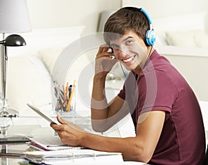 Teenage Boy Studying At Desk In Bedroom Using Digital Tablet