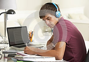 Teenage Boy Studying At Desk In Bedroom Wearing Headphones