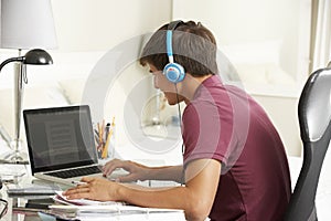 Teenage Boy Studying At Desk In Bedroom Wearing Headphones